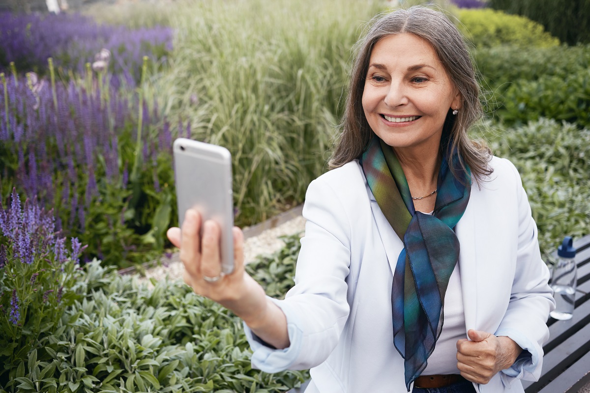  Outdoor picture of joyful stylish female with silk scarf around her neck taking selfie