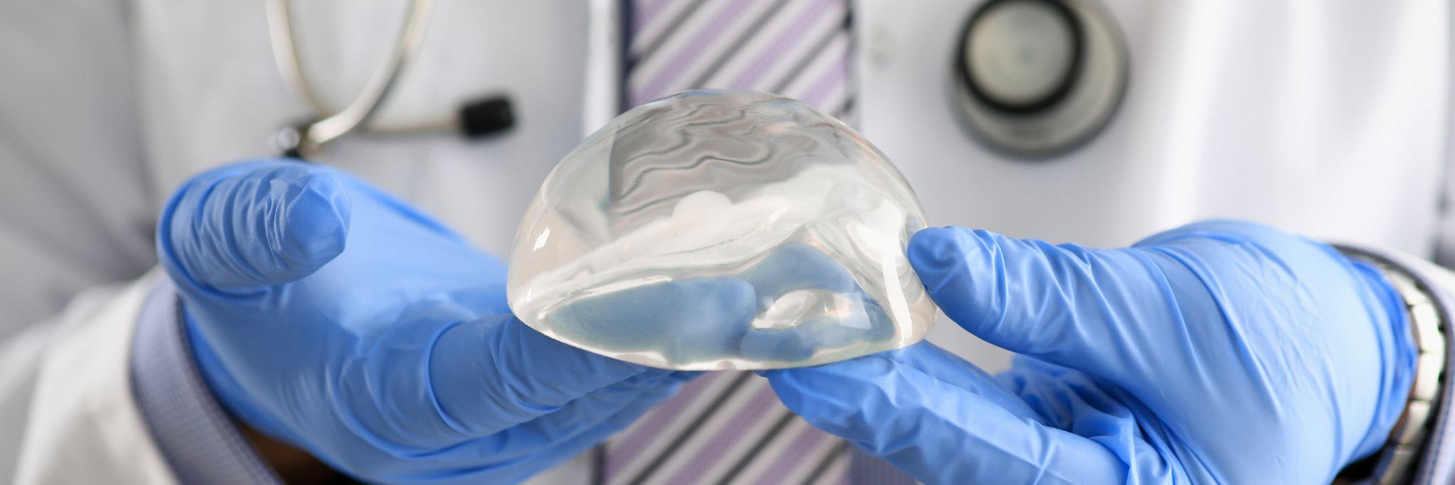 Male doctor hand in blue protective gloves hold new fashion silicone breast implant closeup.