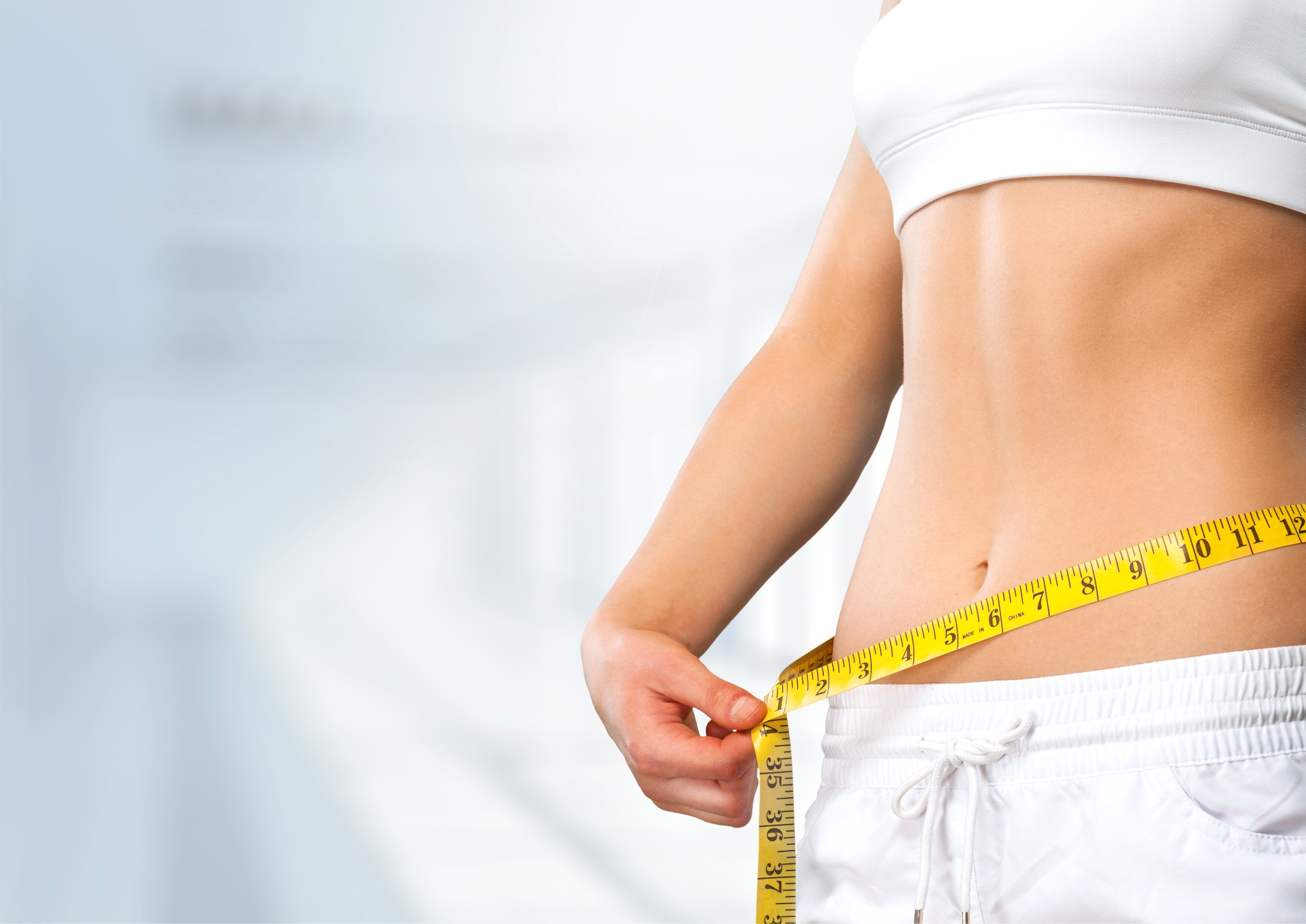 Slim young woman measuring thin waist with a tape measure